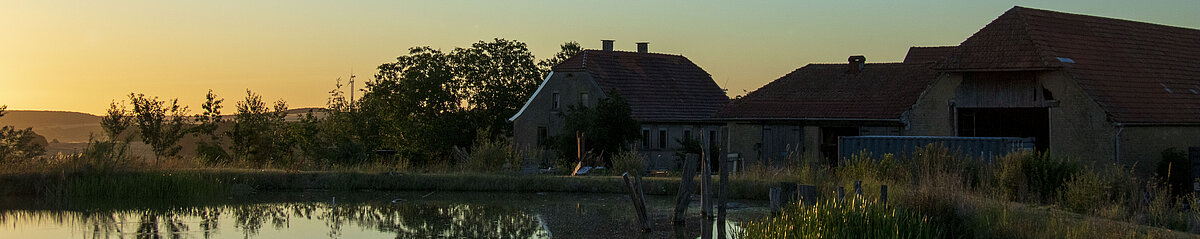 Humusland Hof in der Nordpfalz – Hofgebäude spiegeln sich im Teich bei Abenddämmerung